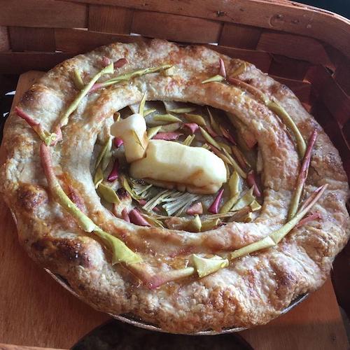 An apple pie with a deer carved out of apple in the center nestled atop apple skin leaves